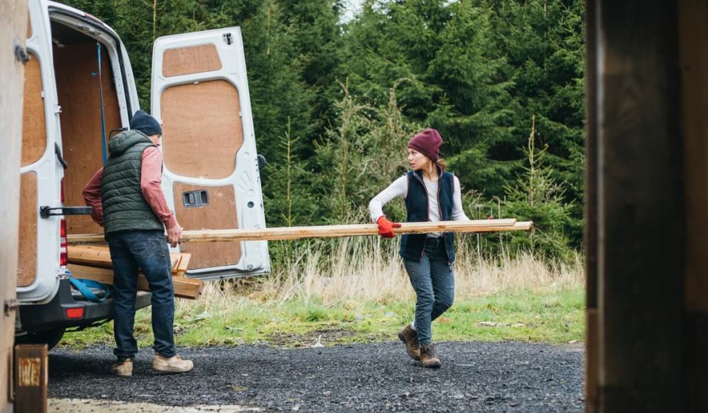 A man and woman carry wood slats out of a truck.