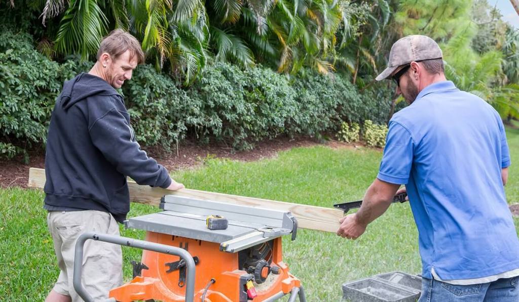 Two contractors using a table to cut a plank of wood