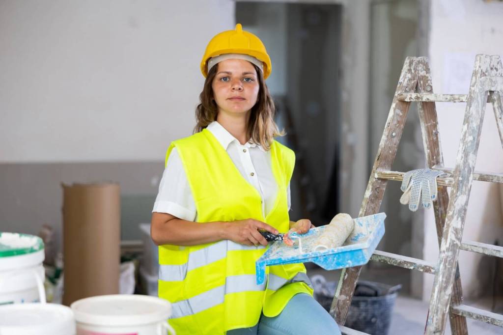 Woman in a hard hat holding a paint roller and tray